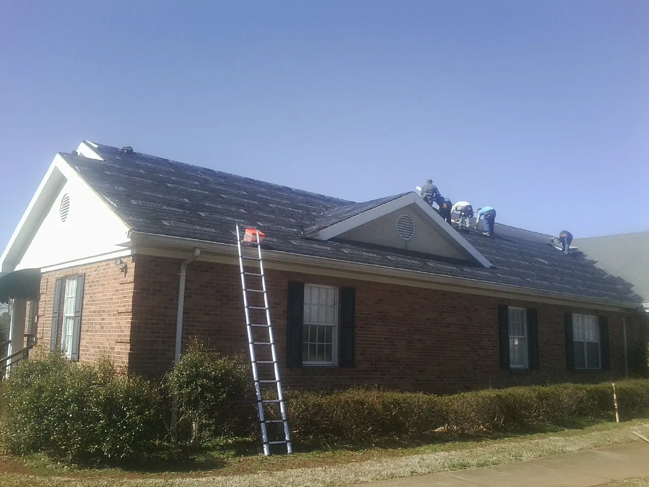 Crew tearing shingles off a brick ranch roof with a ladder set — Metal Roof Repair work by our crew in Clarendon Hills