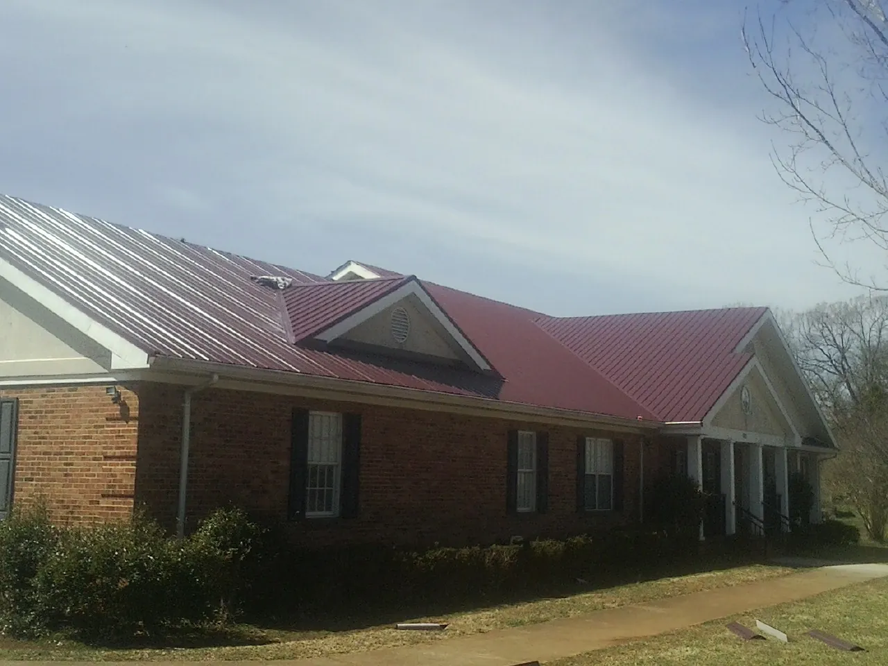 Red metal roof with gabled entries on a long brick building, from a Hail Damage Roof Repair job in Clarendon Hills