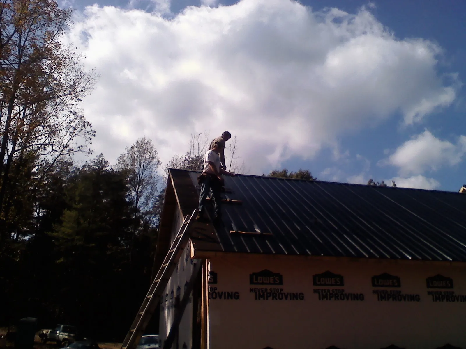 Roofer fastening dark metal panels high against a cloudy sky, from a Roof Inspection job in Clarendon Hills