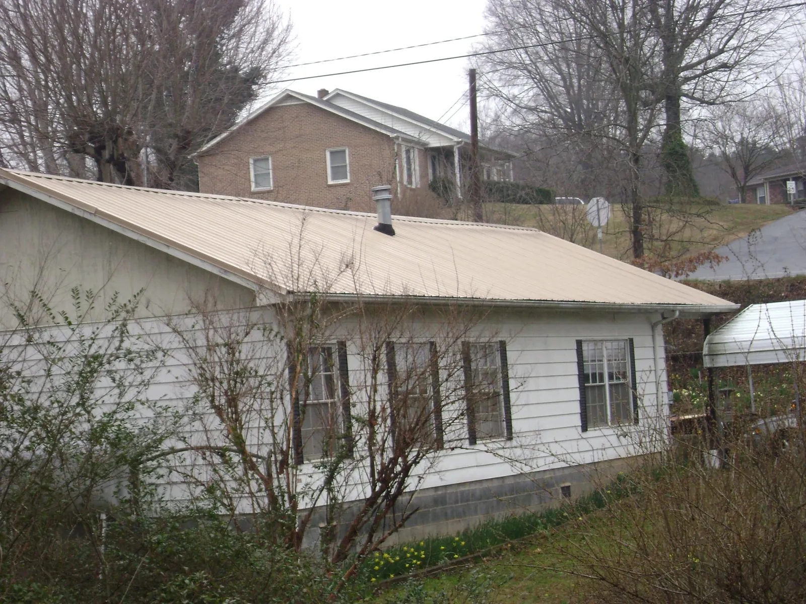 Tan metal roof on a white sided house set into a hillside — Commercial Roofing by Roofing Brothers in Clarendon Hills